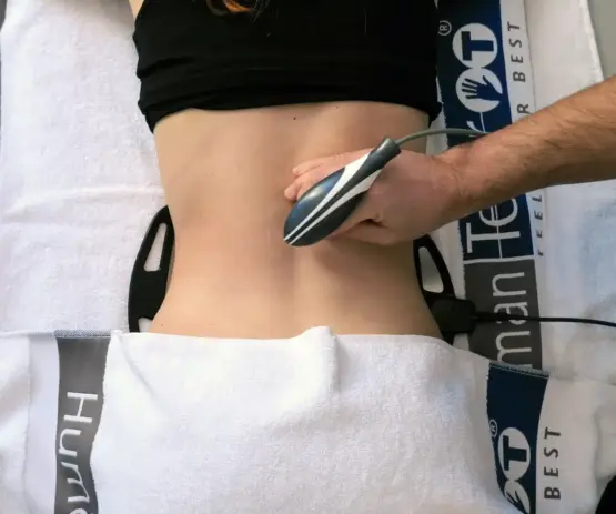 una persona è sdraiata a faccia in giù con un dispositivo portatile applicato alla parte bassa della schiena durante un trattamento. asciugamani con la scritta {{brizy_dc_image_alt imageSrc=